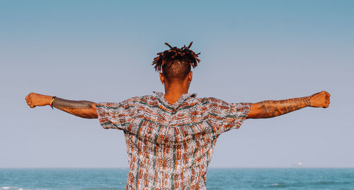 Rear view of man with arms outstretched against clear sky