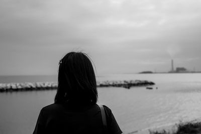 Rear view of woman standing at beach against cloudy sky