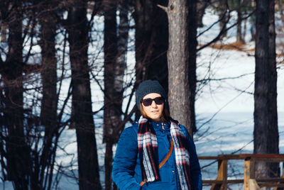 Portrait of woman standing against bare trees during winter