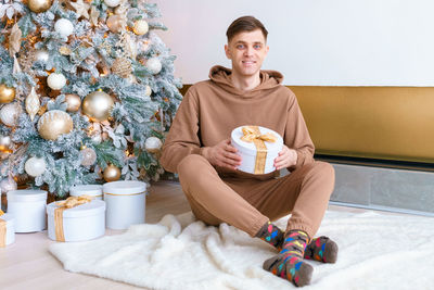 Smiling young man at christmas near christmas tree sitting on floor in cozy