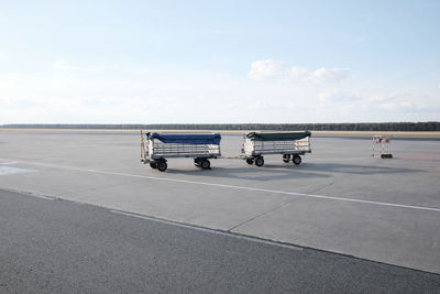 Luggage carts at airport runway against sky