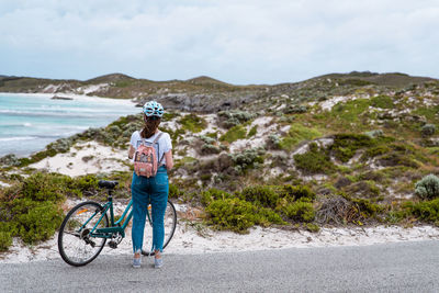 Woman riding bicycle on road by sea against sky