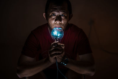 Close-up of man holding illuminated lighting equipment against wall