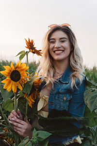 Portrait of smiling young woman with sunflowers against clear sky