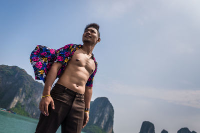 Man wearing fully unbuttoned shirt while standing against sky