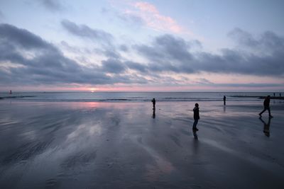 People playing on beach against sky during sunset