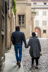 Rear view of two people walking in front of building