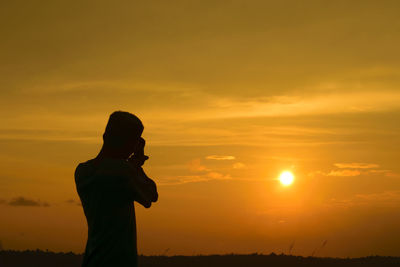 Silhouette man photographing idyllic sunset