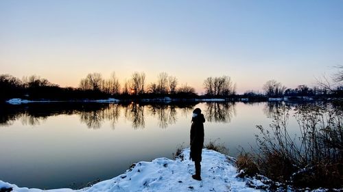 Rear view of man standing by lake against sky during winter