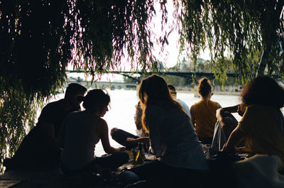 Silhouette people sitting on shore against trees