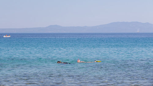 People swimming in sea against clear sky