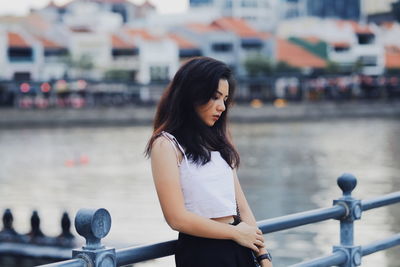 Side view of thoughtful young woman standing on footbridge by river