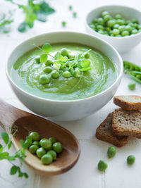 Fresh green pea soup bowl on white tile background