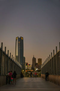 People walking on modern buildings against clear sky at dusk