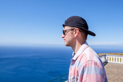 Portrait of young man looking at sea against clear blue sky