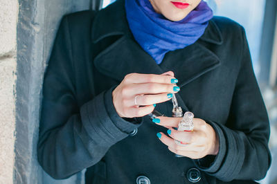 Midsection of young woman smoking while standing by built structure