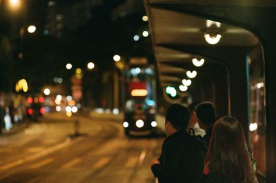 Rear view of people walking on illuminated street at night