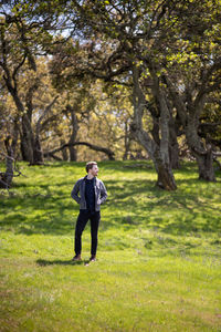 Full body portrait of young man casually dressed outdoors with trees