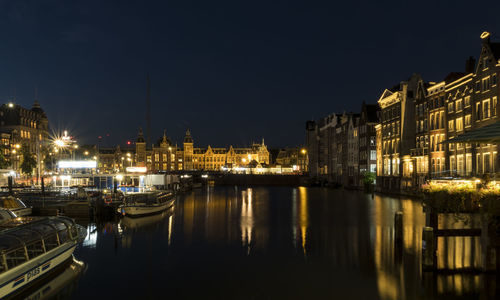 Sailboats moored on river by illuminated buildings in city at night