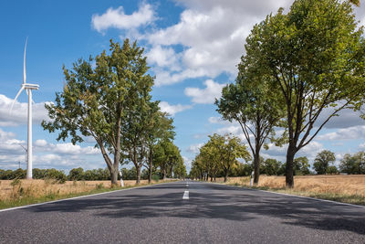 Empty road amidst trees against sky