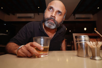 Mature man holding drink looking way while sitting at bar