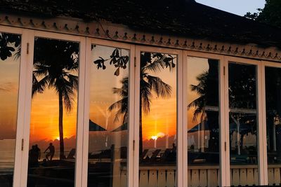 Silhouette trees by building against sky during sunset