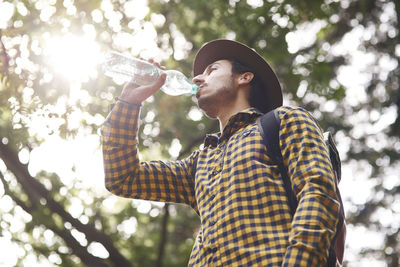 Low angle view of man drinking water from bottle in forest