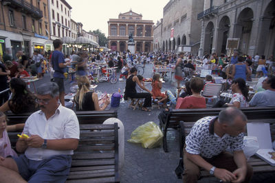 People sitting on street amidst buildings in city