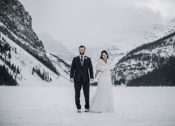 Newlywed couple stand on frozen lake louise, alberta canada in winter