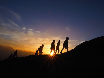 Silhouette people standing on land against sky during sunset