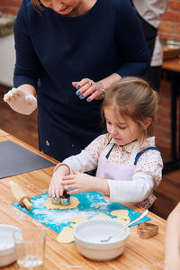 Midsection of woman assisting girl preparing cookie