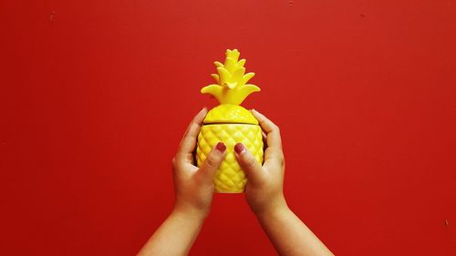 Cropped hands of woman holding artificial pineapple against red background