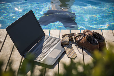 Laptop with tie and shoes at poolside