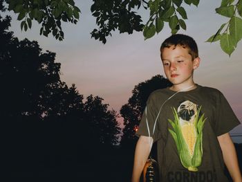 Boy standing against trees during sunset