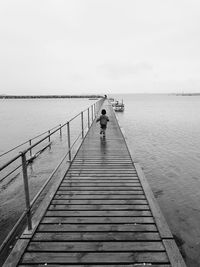 Rear view of boy walking on pier over sea against sky