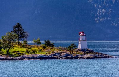 Lighthouse by sea and buildings against sky