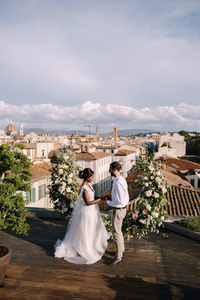 Newlywed couple embracing against cityscape