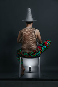 Rear view of man sitting on chair against black background