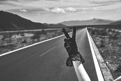 Cropped hand wearing glove while showing peace sign against road