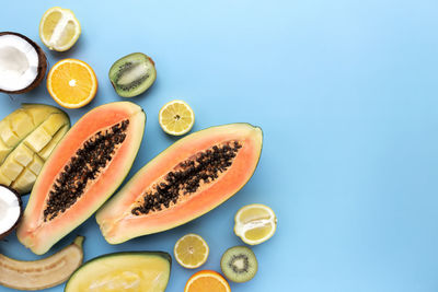 Different fresh tropical cut fruits on blue background. papaya, orange, banana, coconut, mango, kiwi