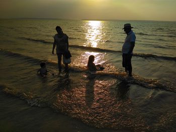 People at beach against sky during sunset