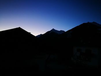 Silhouette houses by mountains against clear sky