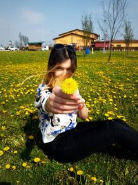 Portrait of young woman holding flower while sitting on grassy field