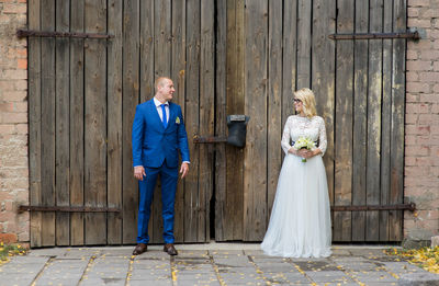 Smiling bridal couple looking at each other while standing against door of barn