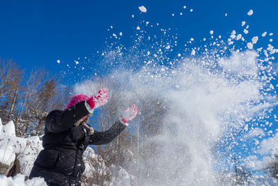 Child throwing snow into the sky on a clear winter day