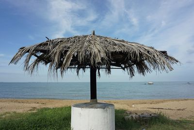 Thatched roof on wooden post on beach against sky