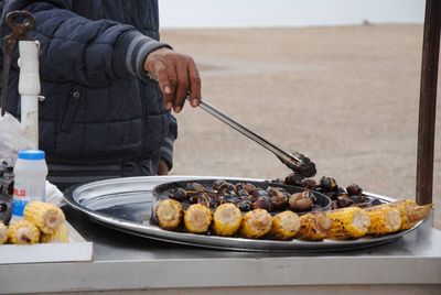 Midsection of vendor holding serving tongs by food at market stall