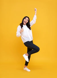 Portrait of young woman standing against yellow background