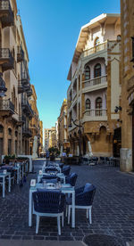 Empty chairs and tables in street amidst buildings in city