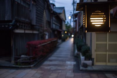 Illuminated street light on footpath amidst buildings at night